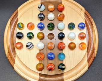 Puede incluir: Un tablero de juego de madera con una superficie de juego circular y un borde rayado marrón y blanco. El tablero está lleno de canicas de colores en un patrón.