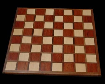 May include: A wooden chessboard with alternating squares of light and dark wood. The board is made of a light wood with a reddish brown stain.