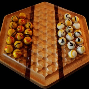 May include: A wooden game board with a honeycomb pattern and two sets of marbles. One set is yellow with black and red swirls, and the other set is white with black swirls.