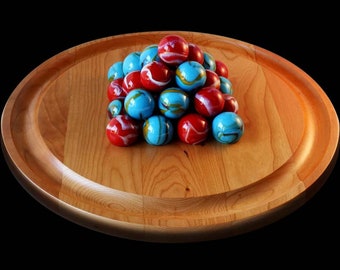 Puede incluir: Una bandeja de madera con un montón de canicas rojas y azules. Las canicas están dispuestas en forma de pirámide.