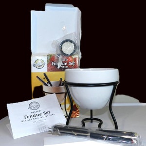 May include: A white ceramic fondue pot with a black metal stand and four fondue forks. The pot is on a white surface with a box and instructions for the fondue set. The box is white with black text that says "Dessert Fondue Set" and "Use and Care Instructions".