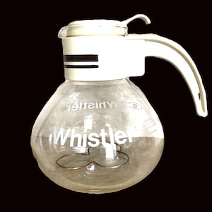 May include: A white and clear glass whistling tea kettle with a white plastic handle and lid. The kettle has the word "Whistler" printed on the side.