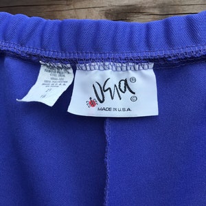 Pode incluir: Uma cal&ccedil;a roxa com uma etiqueta branca que diz "Vera-Tex 100% Poli&eacute;ster Feito nos EUA" e um logotipo de joaninha vermelha com o texto "Usna" e "Feito nos EUA."