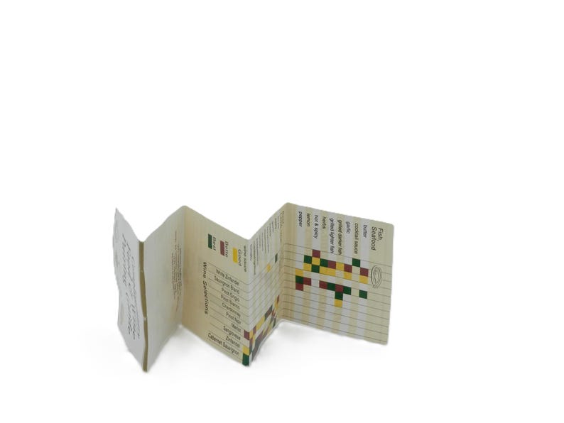May include: A folded paper wine and food pairing guide. The guide is cream-colored with black text and colorful pixelated graphics. The guide lists wine selections and seafood options with suggested pairings.