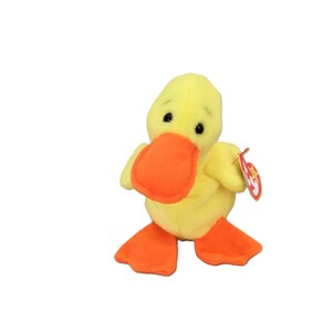 May include: A yellow plush duck with an orange beak and feet. The duck has black eyes and a red beanie baby tag.