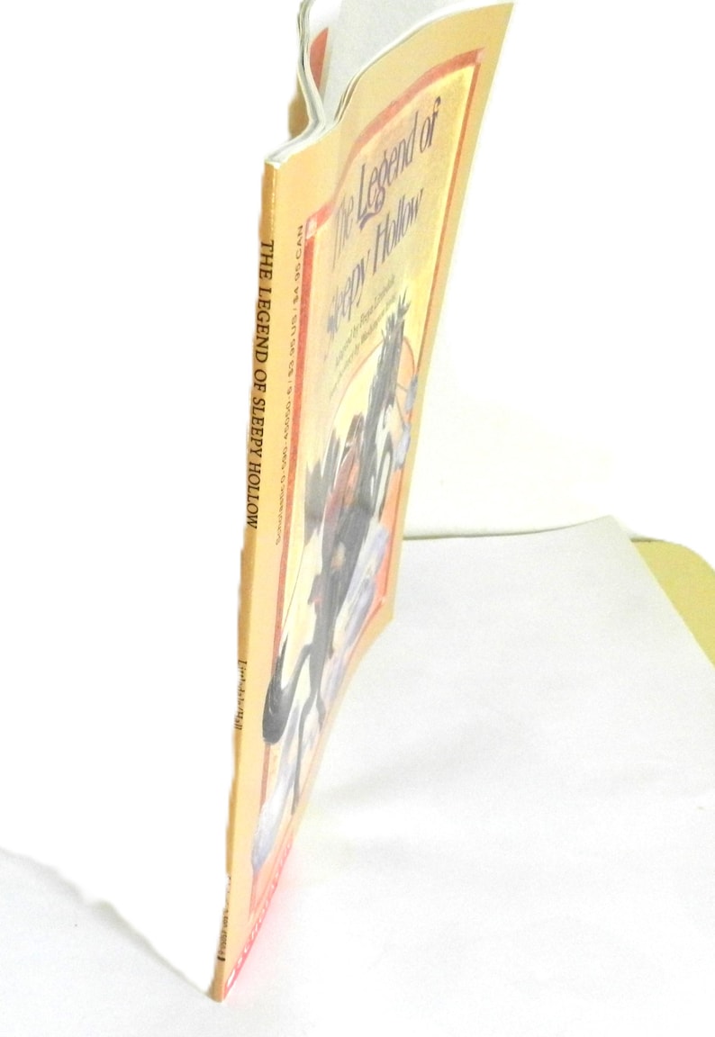 May include: The Legend of Sleepy Hollow book cover with a yellow background and a black and white illustration of a man riding a horse with a headless horseman in the background.