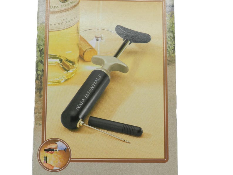 May include: A black and gray wine opener with the text "NAPA ESSENTIALS" printed on the handle. The opener has a lever design and a small, black, cylindrical tool. The image also shows a wine bottle and a wine glass.