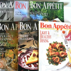 May include: A collection of vintage Bon Appétit magazines. The covers feature various themes, including "City Style," "Cool Delights," and "Light & Healthy Dining." The magazines are stacked, showcasing colorful images and text.
