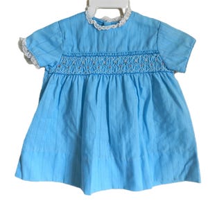 May include: A light blue smocked dress with short sleeves and a white lace trim around the neckline.