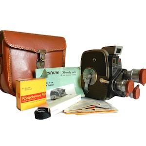 May include: A vintage brown leather camera case with a metal clasp, a black and silver 8mm film camera with a red lens, a roll of Kodakchrome 40 color slide film, and a green and white instruction booklet for a Keystone Twenty Six 8mm movie camera.