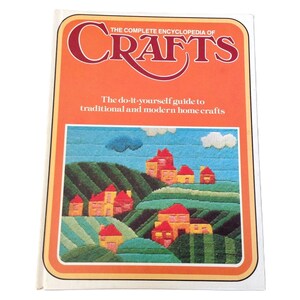 May include: The Complete Encyclopedia of Crafts book cover features a colorful illustration of a village with houses and hills, with the title "The Complete Encyclopedia of Crafts" in red letters.