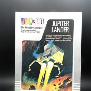 May include: A rectangular game box for the VIC-20 computer titled Jupiter Lander. The cover features a space landing craft illustration, the text VIC-20 The Friendly Computer, and a description of the authentic space landing simulation game.