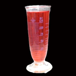 May include: A clear glass graduated cylinder with a red liquid inside. The cylinder has markings in milliliters (ml) from 25 to 125. The cylinder has a wide base and a narrow top.