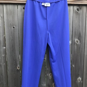 Pode incluir: Uma cal&ccedil;a roxa de perna reta e cintura larga. A cal&ccedil;a est&aacute; pendurada em um cabide dourado contra um fundo de madeira.