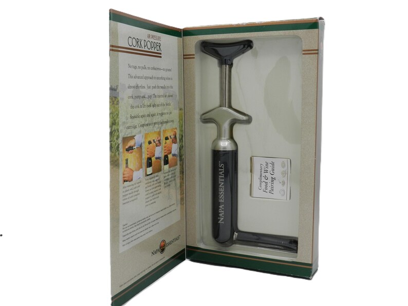 May include: A boxed Napa Essentials cork popper. The wine opener is silver and black, with the words "NAPA ESSENTIALS" printed on the side. The box includes a food and wine pairing guide.