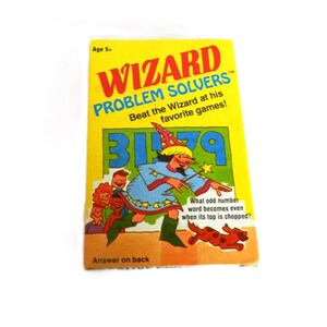 May include: A yellow and red vintage "Wizard Problem Solvers" game box. The box features a cartoon wizard illustration and the text "Beat the Wizard at his favorite games!" The game is for ages 5+.