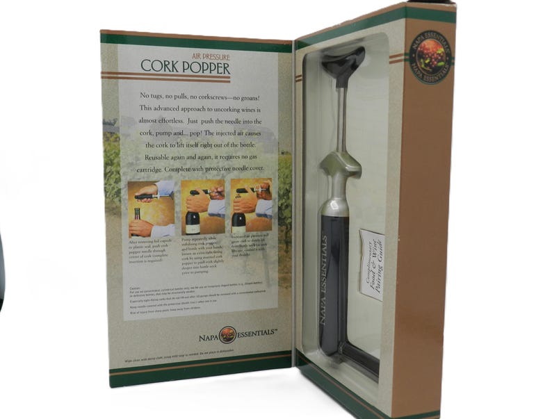 May include: A boxed Napa Essentials air pressure cork popper. The box is tan and green with text and illustrations. The cork popper is silver and black. The text on the box reads "Air Pressure Cork Popper".