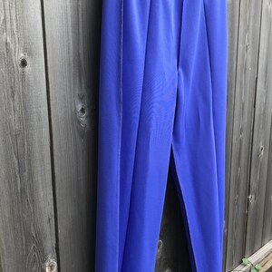 Pode incluir: Uma cal&ccedil;a azul de perna reta e cintura larga. A cal&ccedil;a est&aacute; pendurada em um cabide de madeira contra uma cerca de madeira.