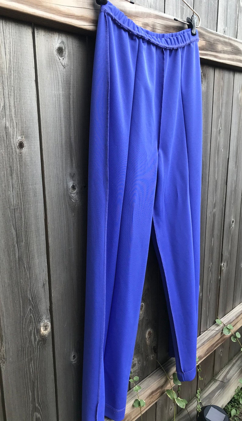 Pode incluir: Uma cal&ccedil;a azul de perna reta e cintura larga. A cal&ccedil;a est&aacute; pendurada em um cabide de madeira contra uma cerca de madeira.