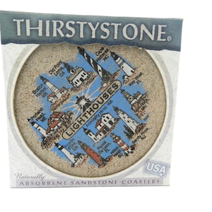 May include: A round, beige sandstone coaster featuring a graphic print of various lighthouses and the text "LIGHTHOUSES" in the center. The coaster is housed in a white cardboard box labeled "THIRSTYSTONE" and "Naturally ABSORBENT SANDSTONE COASTERS".