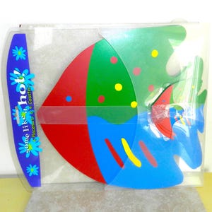 May include: A set of four colorful fish-shaped placemats and coasters. The placemats are red, green, and blue, while the coasters are red and blue. The packaging features the text "some like it hot! 4 Placemats + 4 Coasters".