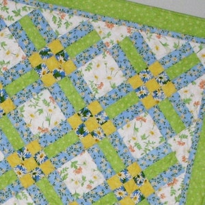 May include: A patchwork quilt with a green, blue, and yellow color scheme. The quilt is made of squares with a floral pattern.