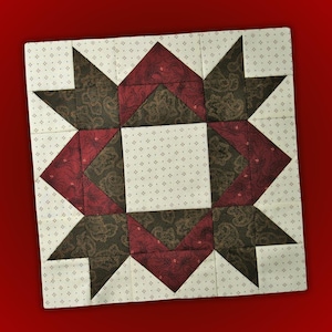 May include: A square quilt block featuring a starburst design. The block is composed of various fabric pieces in shades of burgundy, brown, and cream. The cream-colored fabric has a subtle dotted pattern, while the other fabrics have paisley designs.
