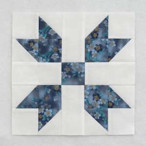 Peut inclure: Bloc de patchwork carré avec un motif floral bleu, turquoise et or sur fond blanc. Le bloc est composé de formes géométriques, créant un design symétrique. Le tissu semble être du coton.