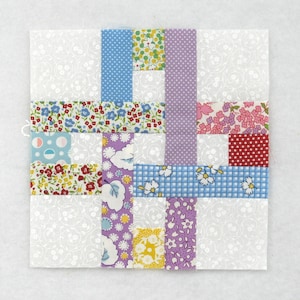 May include: A square quilt block with a white background and a patchwork design. The patchwork features strips of fabric in various colours and patterns, including blue polka dots, floral prints, and a purple dotted stripe. The block is approximately 25 cm square.