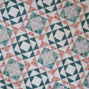 May include: A quilt with a geometric pattern of teal blue and pink triangles. The quilt features a repeating pattern of squares with a floral print and the text "Something Wonderful is Happening" in a white font.