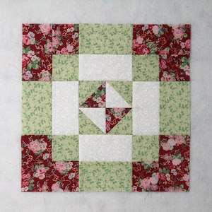 Peut inclure: Un bloc de courtepointe carré avec un motif patchwork. Le bloc incorpore du tissu floral rouge, du tissu à motifs vert clair et du tissu blanc. Le motif comprend des rectangles, des carrés et une forme de losange centrale.