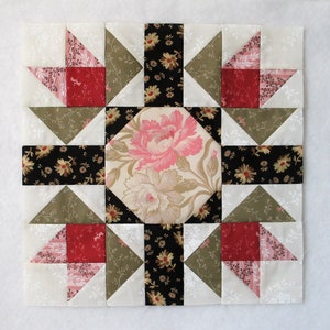 May include: A quilt block with a floral pattern in the center surrounded by a black and white print, a green print, and a white print with pink and red accents.