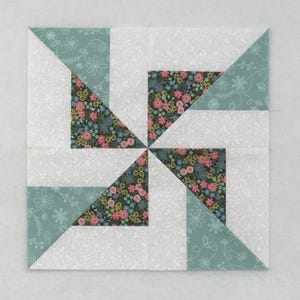 May include: A quilt block with a pinwheel design. The block is made of four different fabrics: a white fabric with a small floral print, a light blue fabric with a white floral print, and two fabrics with a larger floral print in shades of pink, green, and yellow.
