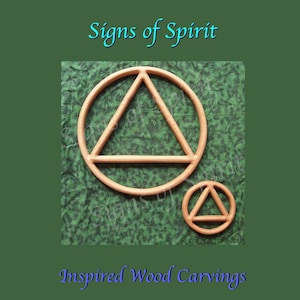 Puede incluir: Dos tallas de madera de un círculo con un triángulo en su interior. La talla más grande es marrón y la más pequeña es de un tono marrón más claro. Las tallas están sobre un fondo verde con el texto "Signs of Spirit" y "Inspired Wood Carvings".