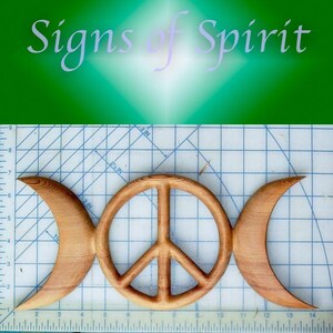 May include: A wooden wall hanging with a peace sign and two crescent moons. The piece is made of light brown wood and is approximately 14 inches wide.