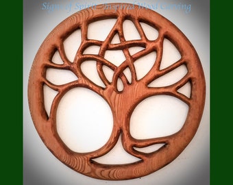 May include: A circular wooden carving of a tree of life with intricate knotwork details. The wood is a light brown colour and the carving is detailed and intricate.