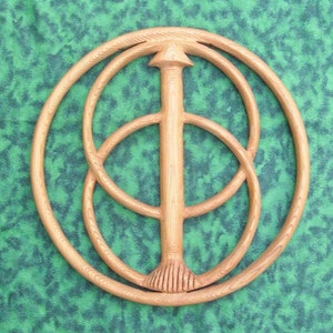 May include: A wooden wall hanging with a circular design featuring three concentric circles and a central vertical piece. The circles are carved with intricate details and the central piece has a pointed top and a decorative bottom.