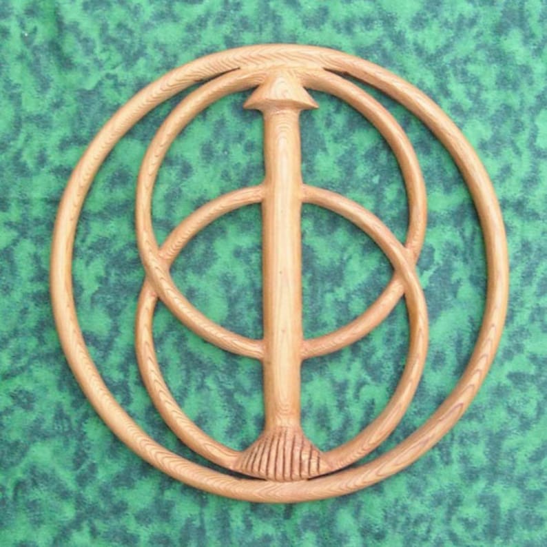 May include: A wooden wall hanging with a circular design featuring three concentric circles and a central vertical piece. The circles are carved with intricate details and the central piece has a pointed top and a decorative bottom.