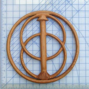 May include: A wooden wall hanging with a circular design featuring three concentric circles and a central vertical post. The circles are made of wood with a natural grain pattern. The post is also made of wood and has a pointed top.