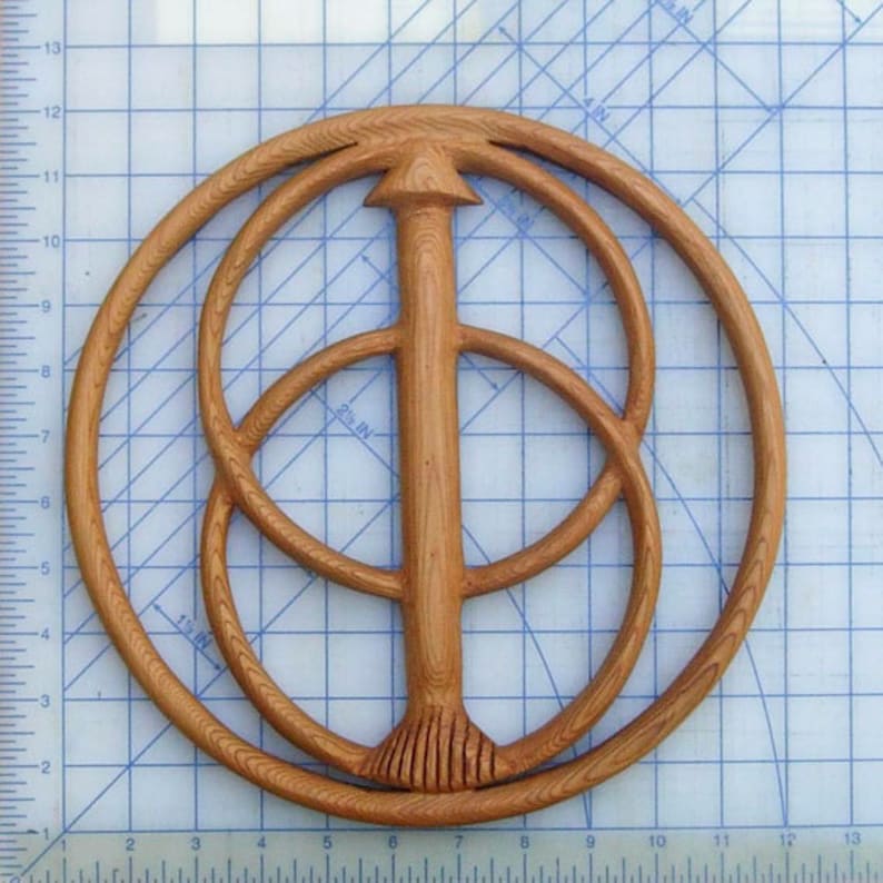 May include: A wooden wall hanging with a circular design featuring three concentric circles and a central vertical post. The circles are made of wood with a natural grain pattern. The post is also made of wood and has a pointed top.