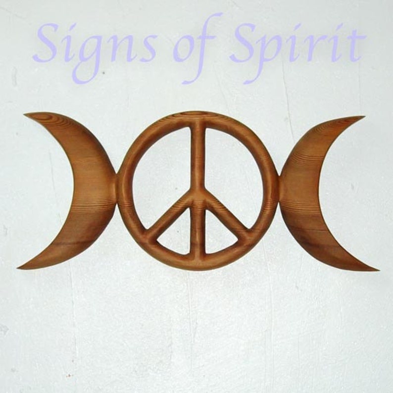 May include: A wooden wall hanging with a triple moon symbol and a peace sign in the center. The symbol is carved from wood and has a natural brown color.