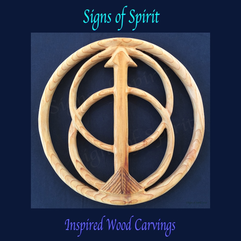 May include: A wooden carving of a circle with an arrow pointing upwards inside. The circle is surrounded by two other circles, creating a layered effect. The carving is a light brown colour and has a smooth, polished finish. The carving is titled "Signs of Spirit" and is described as "Inspired Wood Carvings".