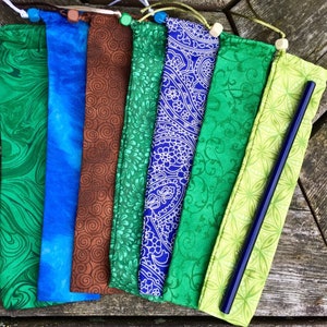 May include: A set of eight colorful fabric pouches with drawstring closures. The pouches are made of different patterned fabrics, including green, blue, brown, and paisley. The pouches are designed to hold reusable straws.