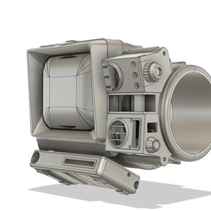 Puede incluir: Modelo 3D detallado de un dispositivo mecánico, posiblemente una cámara o un componente de máquina. El diseño presenta una carcasa rectangular con una lente redondeada, diales y varios elementos mecánicos. El modelo está renderizado en color gris neutro.