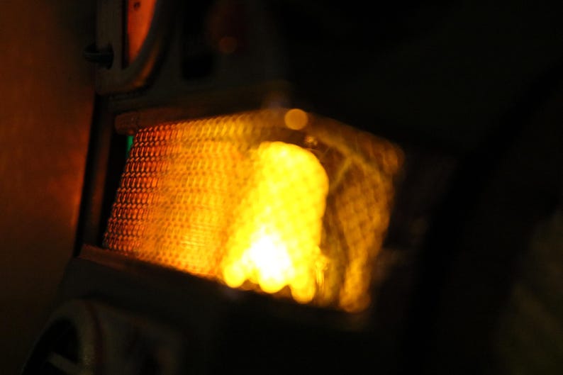 Op de afbeelding: Close-up van een heldere, geel-oranje lichtbron, mogelijk een lamp of warmtebron, met een getextureerde, rasterachtige bekleding. Het licht is diffuus, tegen een donkere achtergrond.