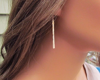 May include: A pair of silver dangle earrings with a hammered texture. The earrings are long and thin, and they hang from a simple hook.