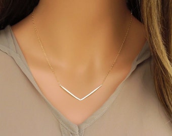 May include: A gold chain necklace with a simple, minimalist V-shaped pendant.