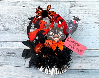 Könnte beinhalten: Ein Halloween-Zentrumstück mit einer schwarzen Katze, einer Hexe und einer Eule, mit einer rot-schwarzen Schleife, orange-schwarzem Lametta und einem Schild mit der Aufschrift "Greetings for Hallowe'en".