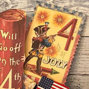 May include: Vintage Fourth of July themed paper cutouts. One cutout features a soldier aiming a rifle with the text "4th of July". Another cutout reads "Will Go off on the 4th". Includes a small American flag.