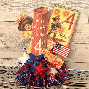May include: A patriotic Fourth of July centerpiece featuring vintage-style illustrations. Includes a woman peeking from behind a firecracker, a soldier, an American flag, and star-shaped decorations in red, white, and blue.